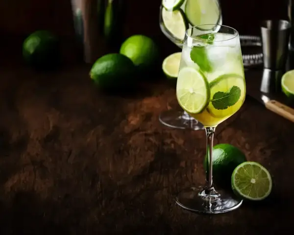 Orzeźwiający Hugo Spritz z limonką i miętą, otoczony świeżymi limonkami na drewnianym blacie.