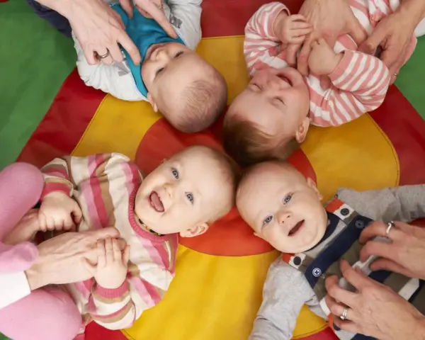 Uśmiechnięte dzieci na kolorowej macie. Czy żłobek jest dobry dla dziecka? Wiele maluchów wesoło bawi się z opiekunami.