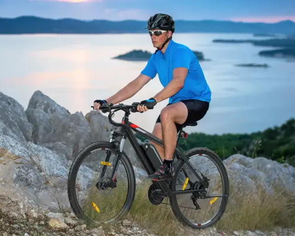 Man riding a mountain bike on a rocky trail overlooking a serene bay at dusk.