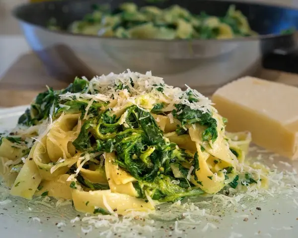 Makaron tagliatelle ze szpinakiem i startym parmezanem, obok kawałek sera.