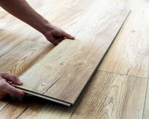 Man's hands placing a laminate plank to repair suelo laminado.