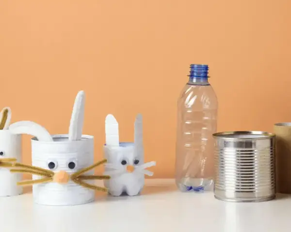 Zające z rolek po papierze i puszek to świetne przykłady recyklingu w życiu codziennym. W tle pusta butelka i rolka po ręczniku papierowym.
