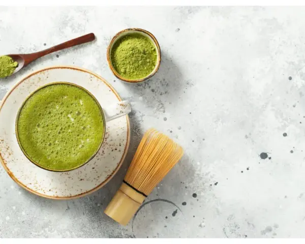 Zielona, spieniona matcha w filiżance, obok bambusowa miotełka i łyżeczka z proszkiem. To właśnie co to matcha – napój pełen energii.