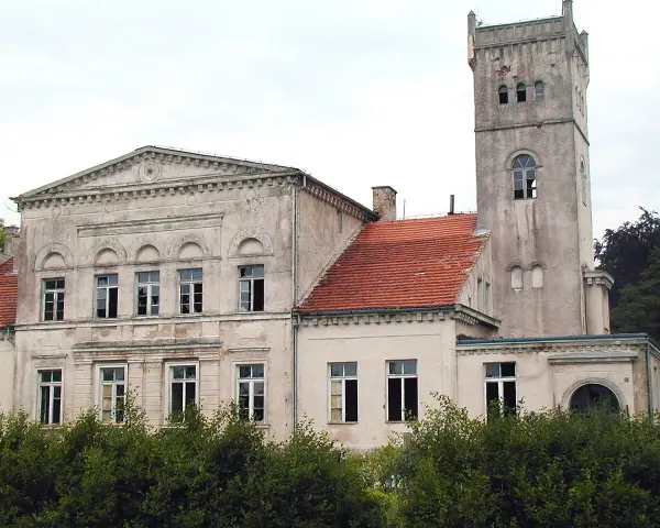 Pałac Rekowo, z wieżą i czerwoną dachówką, otoczony zielenią.