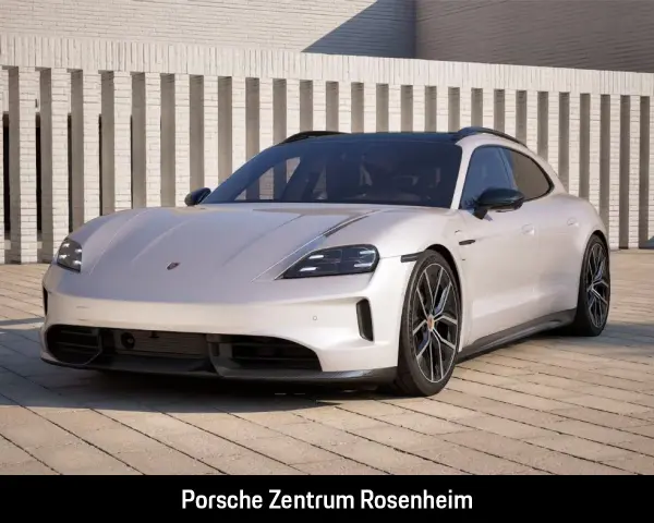 Elegancki Porsche Taycan w kolorze jasnoszarym, zaparkowany przed nowoczesnym budynkiem. Sprawdź porsche taycan cena!