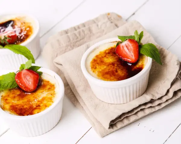 Trzy kremowe desery, Crème brûlée czy crema catalana, ozdobione truskawkami i miętą, kuszą skarmelizowanym cukrem.