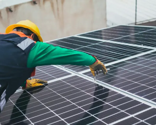 Handwerker mit gelbem Helm montiert Solarmodule für solarstrom einspeisen.