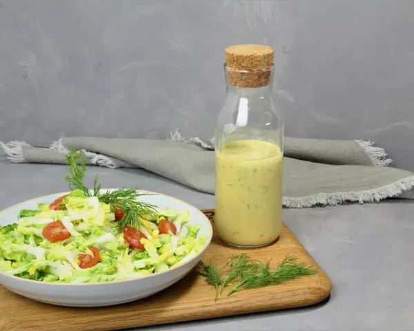 Frischer Salat mit Tomaten und Mais, daneben eine Flasche mit cremigem Jogurt Dressing und Dill.