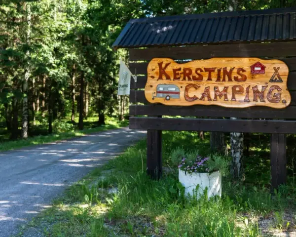Välkommen till Kerstins Camping! En skylt i trä visar vägen till en lugn plats i skogen.