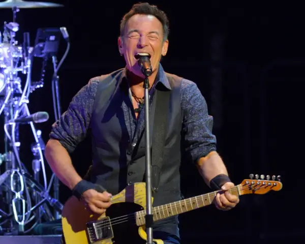 Bruce Springsteen singt und spielt seine ikonische Bruce Springsteen Gitarre auf der Bühne, während die Band im Hintergrund spielt.