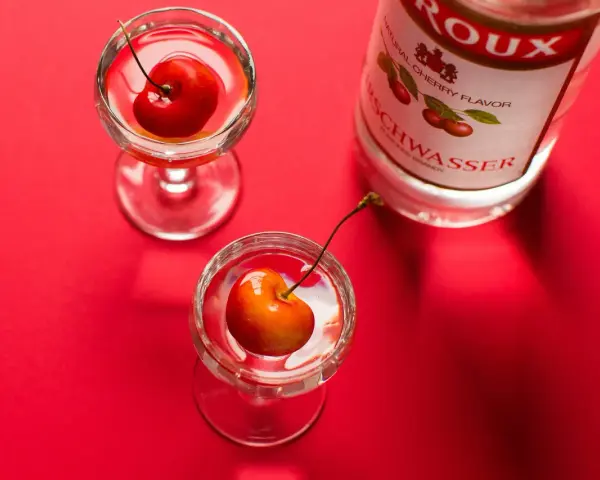 Zwei Gläser mit Kirschen und eine Flasche Kirschwasser auf rotem Hintergrund. Was ist Cherry? Ein süßer Genuss.