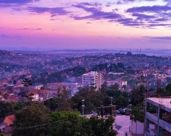 Fioletowe niebo nad krajem z kampalą, z widokiem na wzgórza pokryte zabudowaniami i zielenią.
