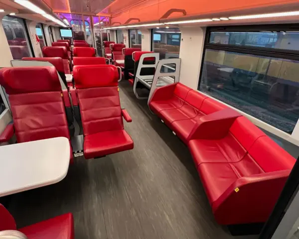 Interior of a modern train, with red leather seats and tables, ready for a journey from AMS to Brussels.