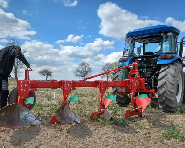 Rolnik przygotowuje pług do orania ziemi. Błękitne niebo z chmurami nad polem.