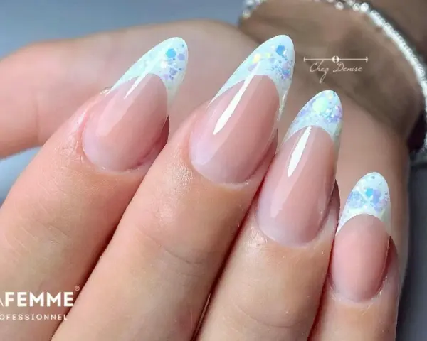 Unghie a mandorla con french manicure rivisitato: base nude e punta bianca con brillantini scintillanti, un tocco di french rosso con brillantini.
