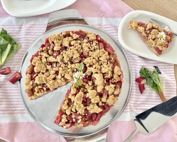 Ein köstlicher Rhabarberkuchen mit Streuseln, garniert mit Gänseblümchen. Frischer Rhabarber und knusprige Streusel machen diesen Kuchen zum Genuss.