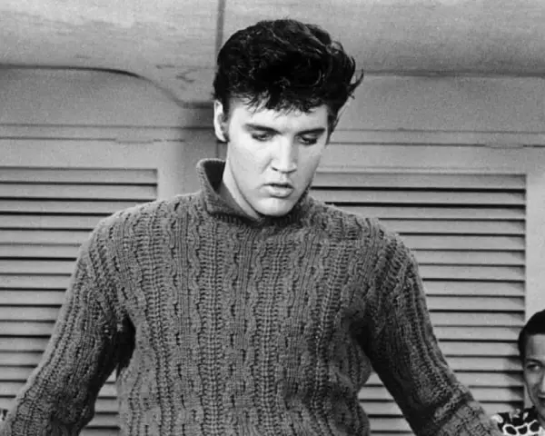 Elvis Presley in einem Strickpullover, vielleicht bei der Aufnahme seines letzten Liedes. Im Hintergrund zwei Männer.