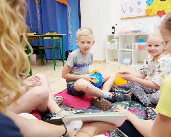 Chłopiec, około 10 lat, siedzi na podłodze z niebieską zabawką. Wokół niego inne dzieci.