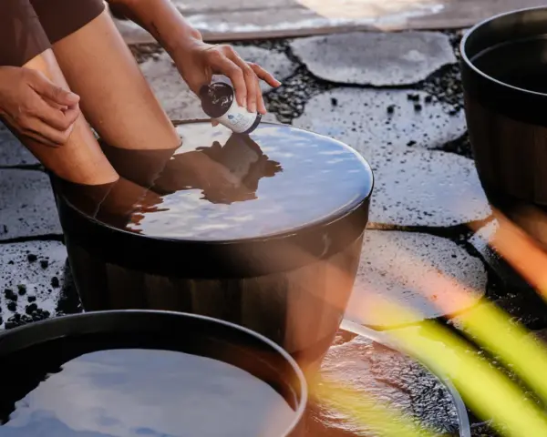 A person adds a few drops from a small bottle to a wooden tub filled with water, creating the best natural foot soak.