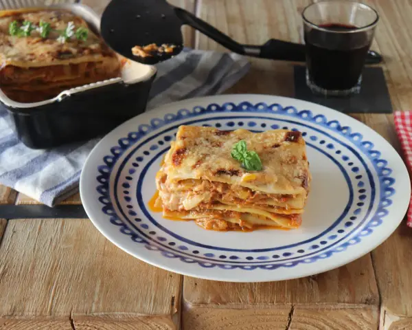 Una porción de lasaña de atún, dorada y gratinada, servida en un plato con diseño azul.