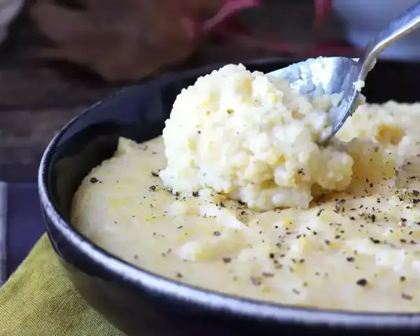Kremowa polenta, idealna do prostego polenta przepis, posypana świeżo mielonym pieprzem, nabierana łyżką z czarnej miski.