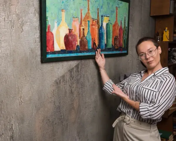 Une femme explique comment vernir un tableau, montrant une œuvre colorée de bouteilles.