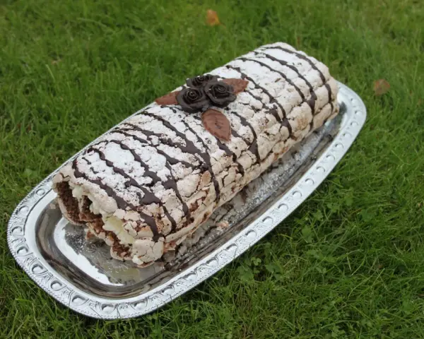 En läcker budapestrulle recept på ett silverfat, dekorerad med chokladrosor och pudersocker, på en grön gräsmatta.