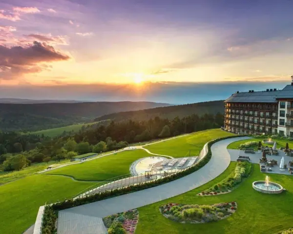Hotel Arłamów z basenem i tarasem, otoczony zielonymi wzgórzami o zachodzie słońca. Ile pokoi ma hotel Arłamów? Tego nie widać, ale jest ich wiele!