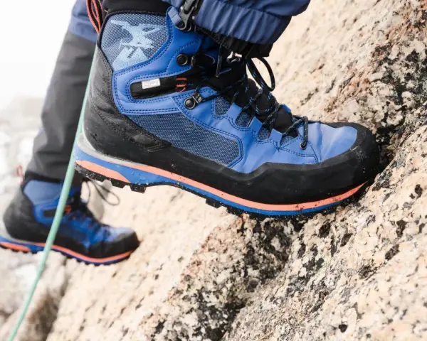 Close-up of a blue and black hiking boot with orange accents, gripping a rocky surface.