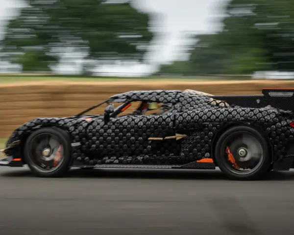 Czarny, pikselowy hypercar z pomarańczowymi akcentami pędzi po torze, tworząc wrażenie ruchu.