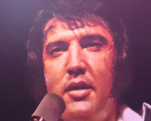 Elvis Presley, sichtlich erschöpft, singt in ein Mikrofon. Ein Moment, der an seinen elvis presley last concert erinnert.