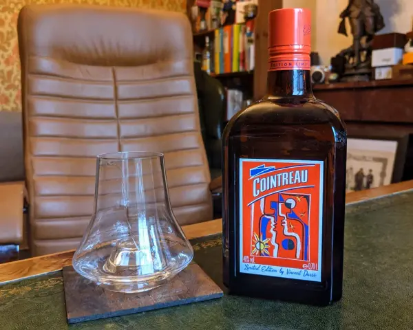 Cointreau kontra Triple Sec w koktajlach: butelka Cointreau i pusty kieliszek na biurku.