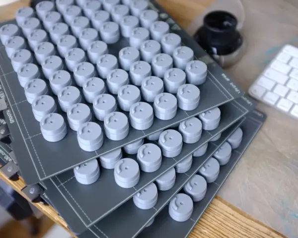 Stosy szarych, cylindrycznych elementów, świeżo po prototypowaniu 3d. Obok klawiatura i kałamarz.