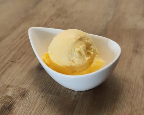 Ein Löffel cremiges Mandarinen Eis in einer weißen Schale auf Holzhintergrund.
