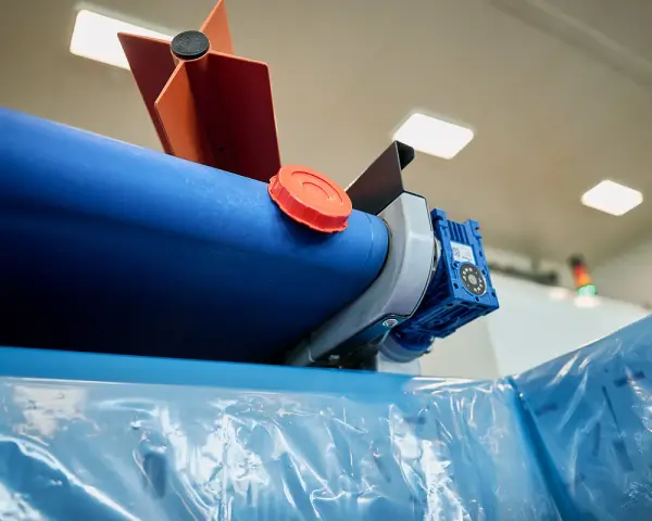 Maszyna do produkcji folii, z niebieskim wałkiem i pomarańczową nakrętką, przygotowuje materiał cerplast do dalszej obróbki.
