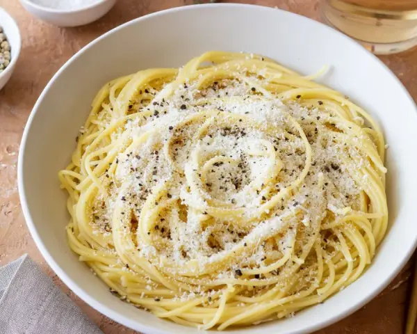 Miseczka spaghetti posypana parmezanem i pieprzem, obok przyprawy i czosnek.