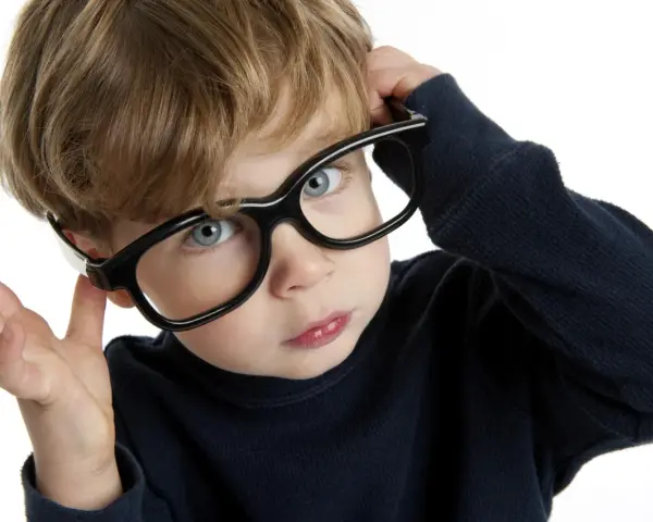 Chłopiec z niebieskimi oczami poprawia okulary, zastanawiając się nad nadwzrocznością u dzieci kiedy okulary są potrzebne.