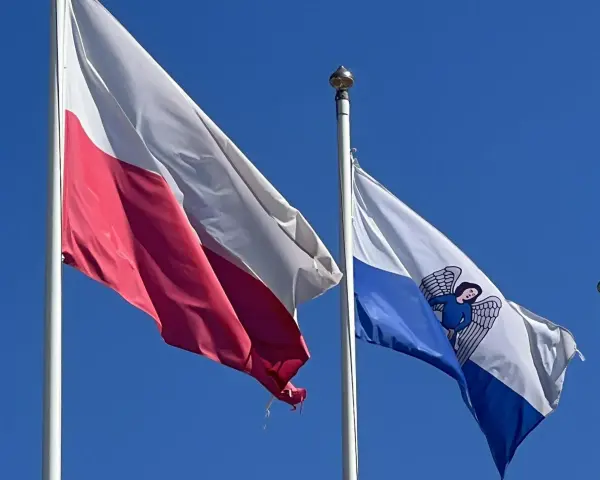 Flaga Torunia i biało-czerwona flaga Polski powiewają na tle błękitnego nieba.