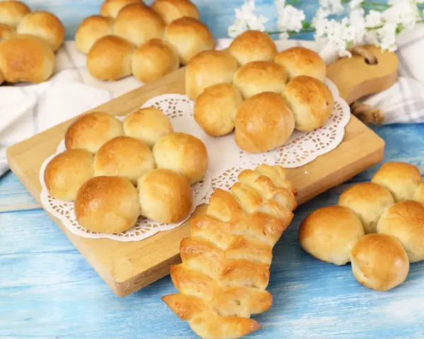 Morbidi panini al latte dorati, alcuni disposti a grappolo su un tagliere, altri su un panno bianco.