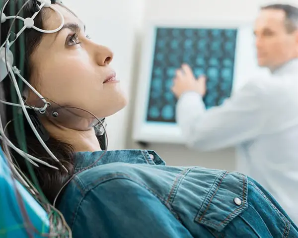 Frau mit EEG-Kappe für eeg medizinische Untersuchung, Arzt deutet auf Bildschirm mit Gehirnscans.