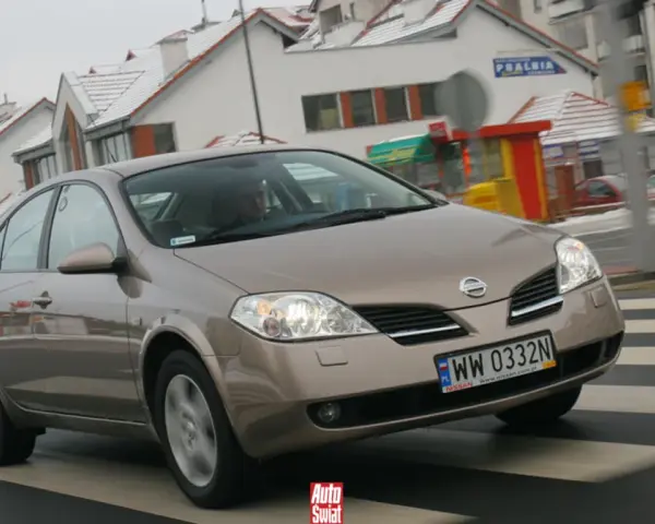 Brązowy Nissan Primera przejeżdża przez pasy na tle zaśnieżonych domów.