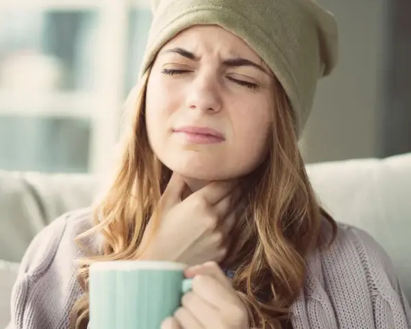 Femme souffrant d'extinction de voix, cherchant un remède miracle avec une tasse chaude.