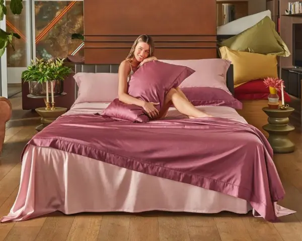 Una donna sorride su un letto con lenzuola rosa. Per mantenerle fresche, si lavano a 40 gradi.