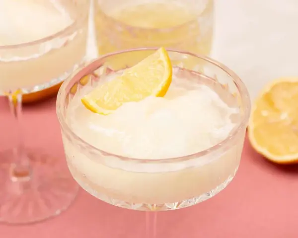 Erfrischendes Limoncello Sorbet in einem Kristallglas, garniert mit einer Zitronenspalte. Ein halbe Zitrone liegt daneben.