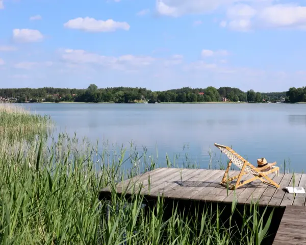 Spokojne kaszubskie jeziora, drewniany pomost z leżakiem i książką, otoczone trzcinami i lasem.