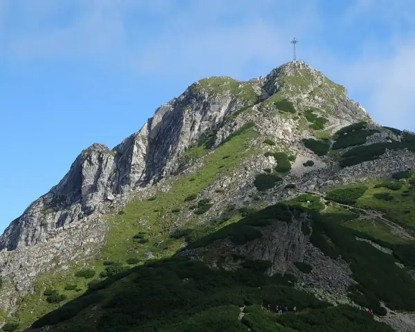 Szczyt Giewontu z krzyżem, zielone zbocza, kamienie i ścieżka. Wjazd na Giewont jest darmowy, ale wymaga wysiłku.