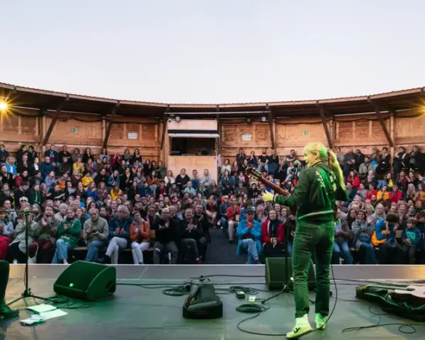 Konzert auf dem Tempelhofer Feld: Eine Musikerin spielt Gitarre vor einem begeisterten Publikum in einem hölzernen Amphitheater. Ein wahrer luftschloss tempelhofer feld Traum.