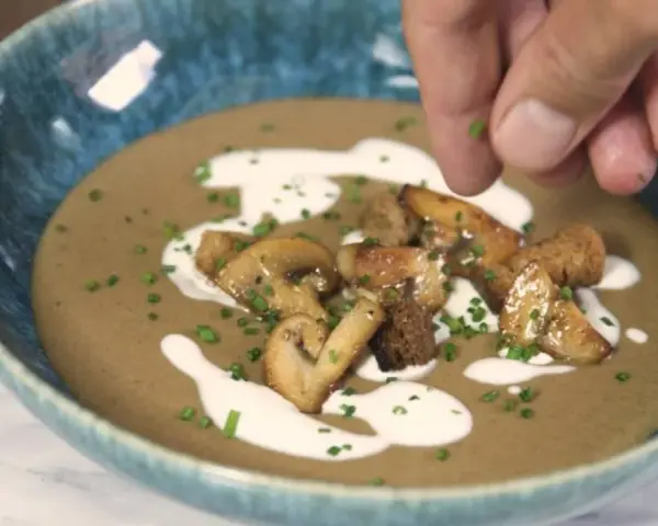 Crema de champiñones servida en un cuenco azul, decorada con champiñones salteados, picatostes y un chorrito de nata.