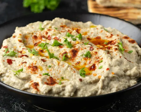 Kremowa pasta z bakłażana, doprawiona papryką i posypana natką pietruszki, w czarnej misce. Idealna do pieczywa.