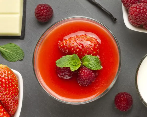 Delizioso dessert con coulis di fragole, fragole fresche, lamponi, menta, cioccolato bianco e un baccello di vaniglia.